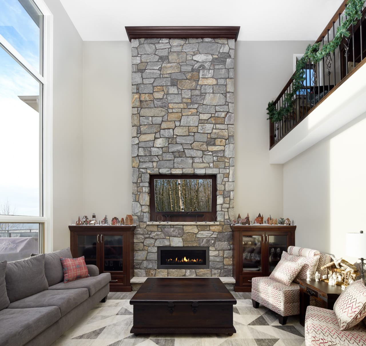 A family room with a tall river rock fireplace with dark brown cabinetry on either side.