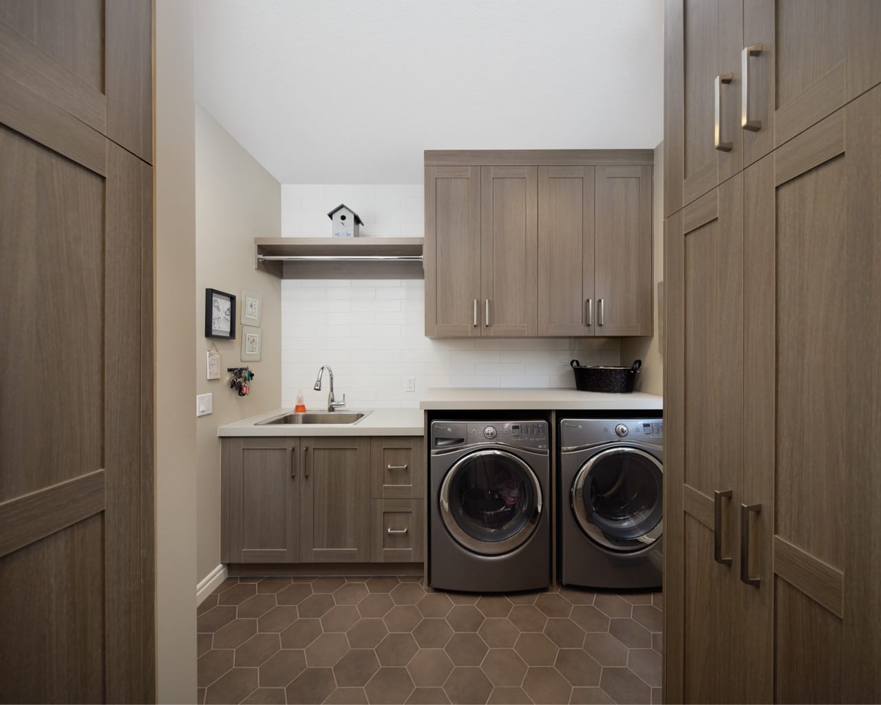 Neutral-toned laundry room with a washer, dryer, sink and cabinetry.