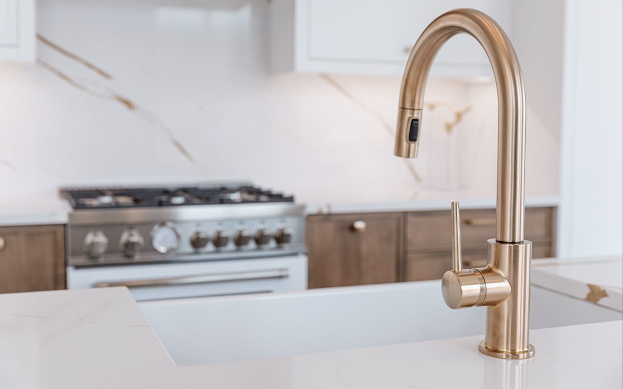 Close up of a gold sink faucet with walnut cabinetry in the background.